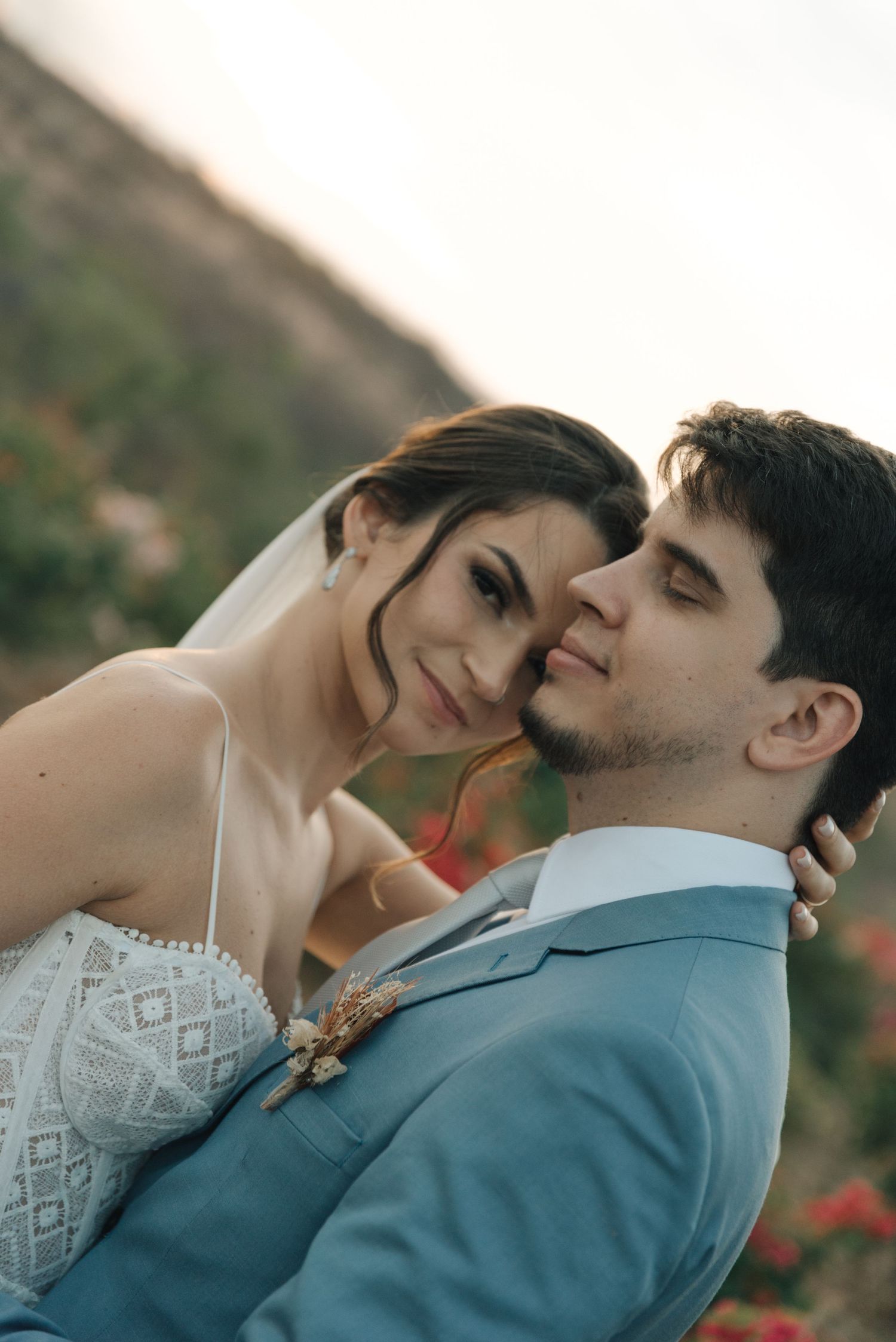Romantic wedding portrait with couple embracing among desert flowers at sunset.