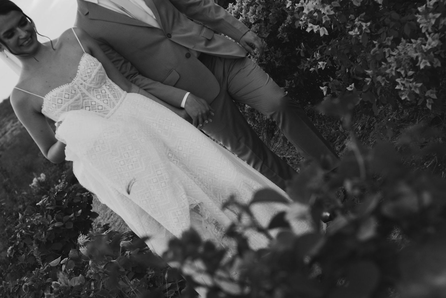 Close-up detail shot of bride's lace dress and groom's suit during outdoor wedding.