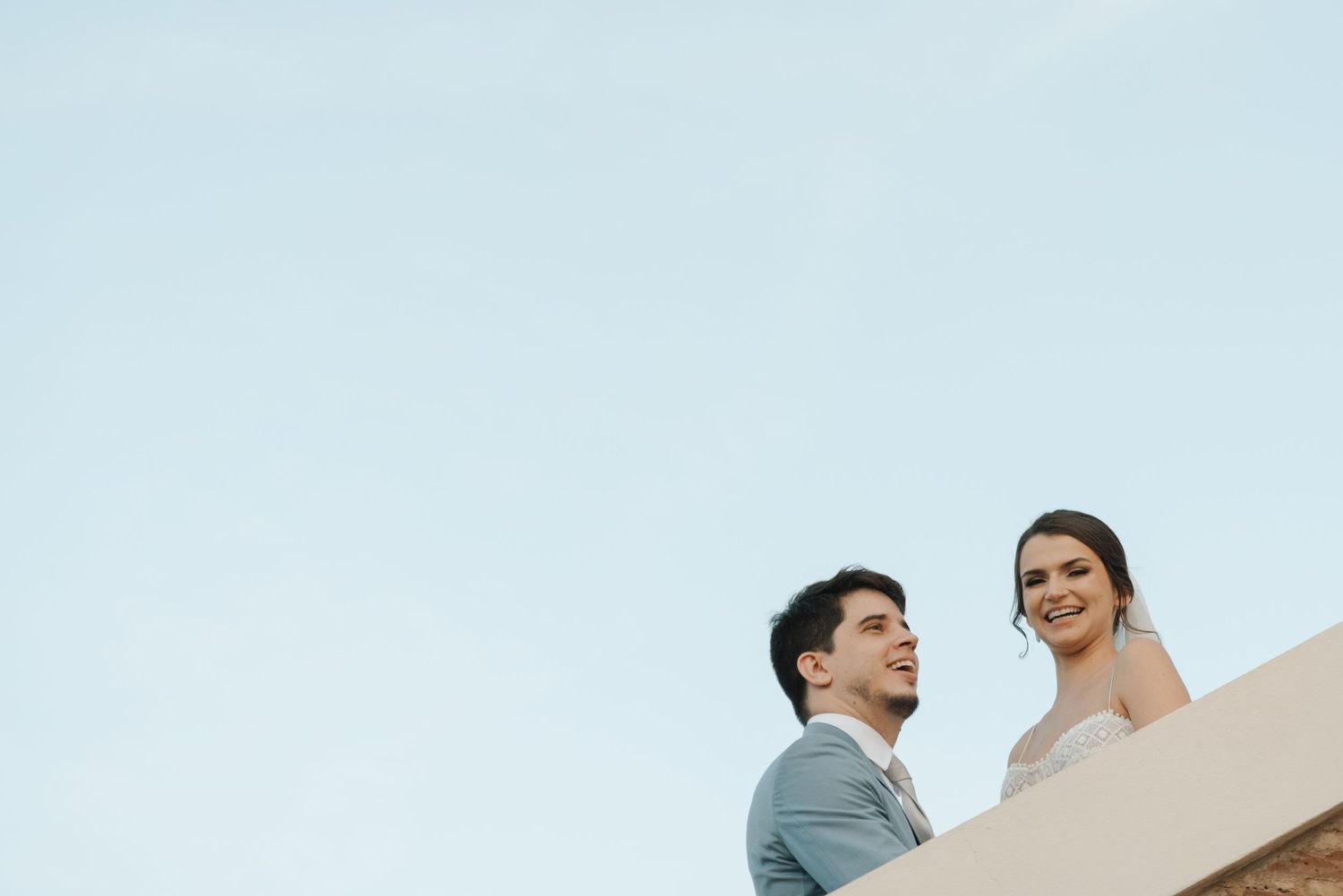 Low-angle architectural wedding portrait of couple against blue sky.