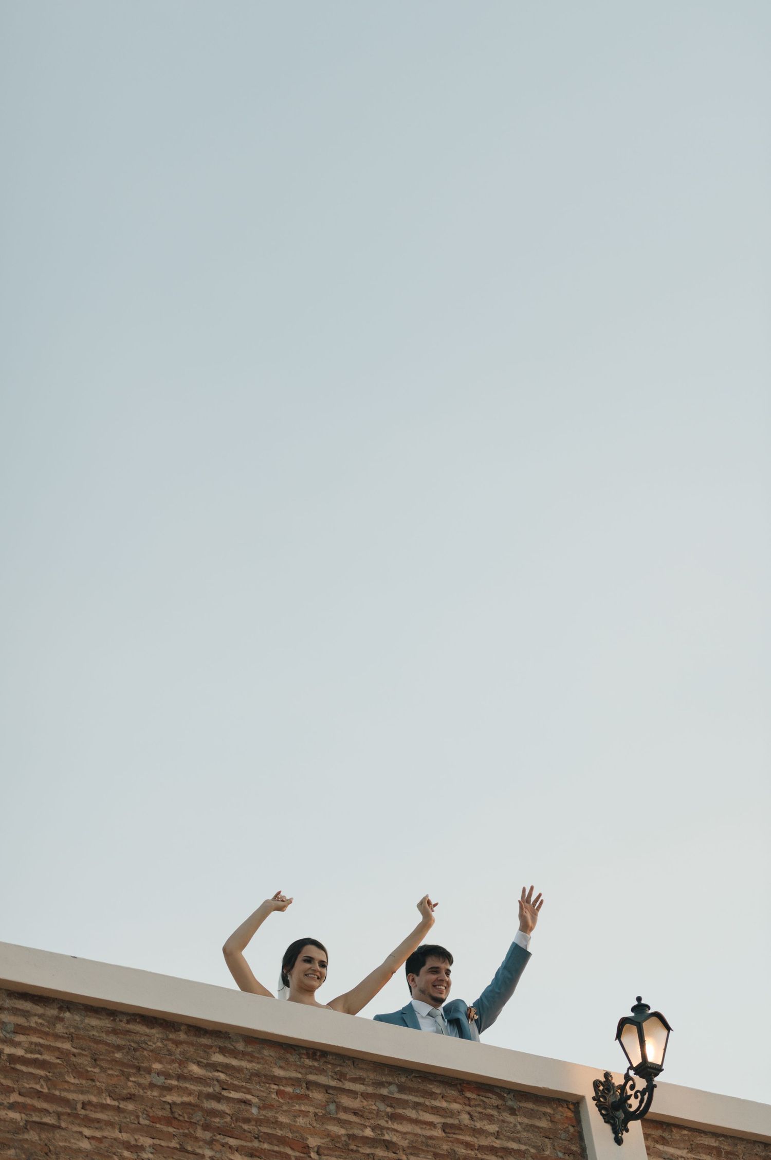 Couple celebrating on a rooftop with raised arms against clear sky with vintage lamp post.
