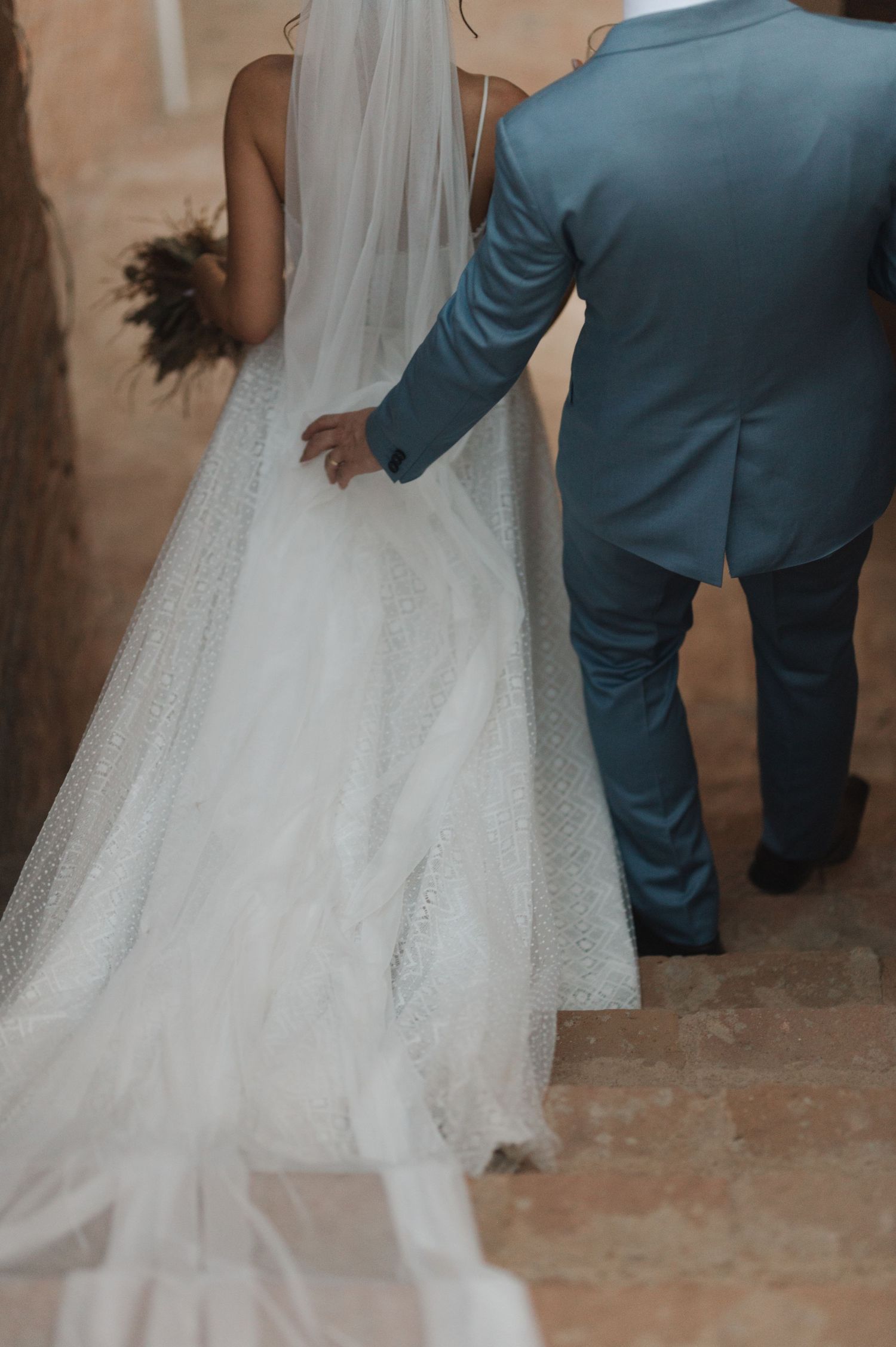 Close-up of bride in flowing white dress with groom in blue suit walking together.