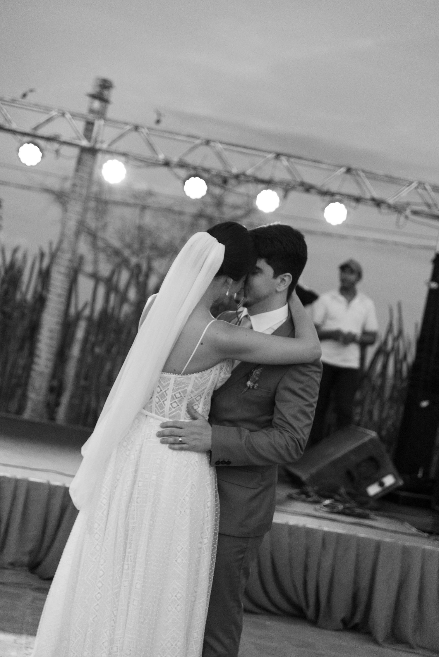 Black and white photo of a couple's first dance under glowing string lights at outdoor reception.