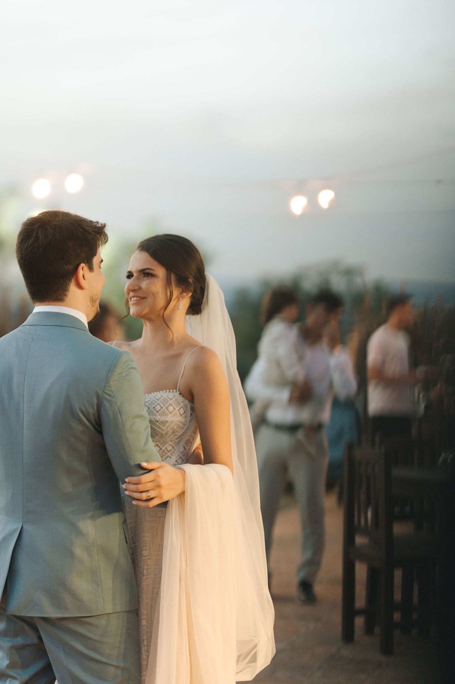 Romantic sunset moment between couple at outdoor wedding reception with string lights.