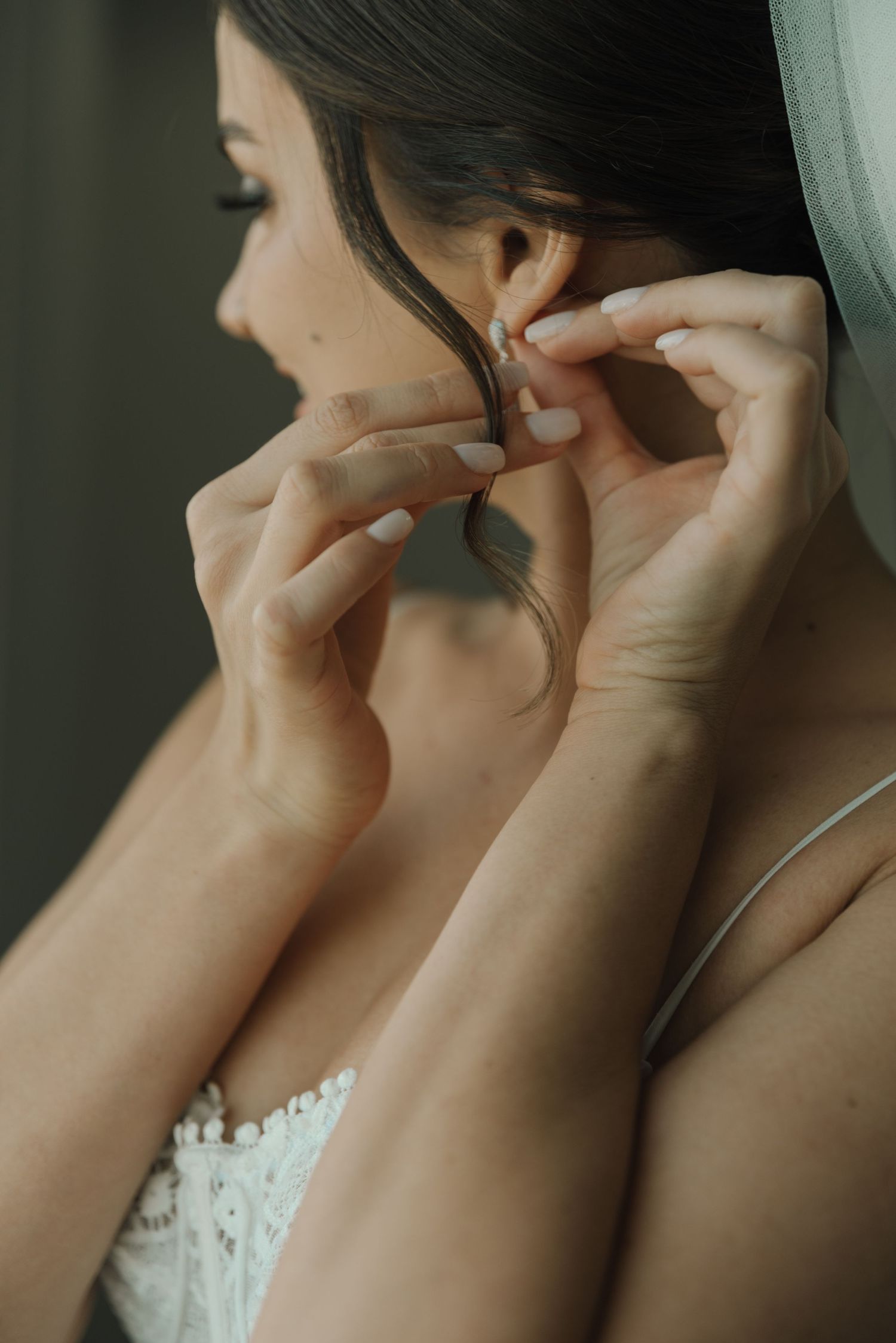 Close-up shot of hands putting on earrings during wedding preparations.