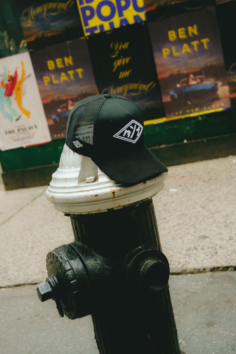 Black baseball cap sits atop a fire hydrant with Ben Platt books displayed in the background.