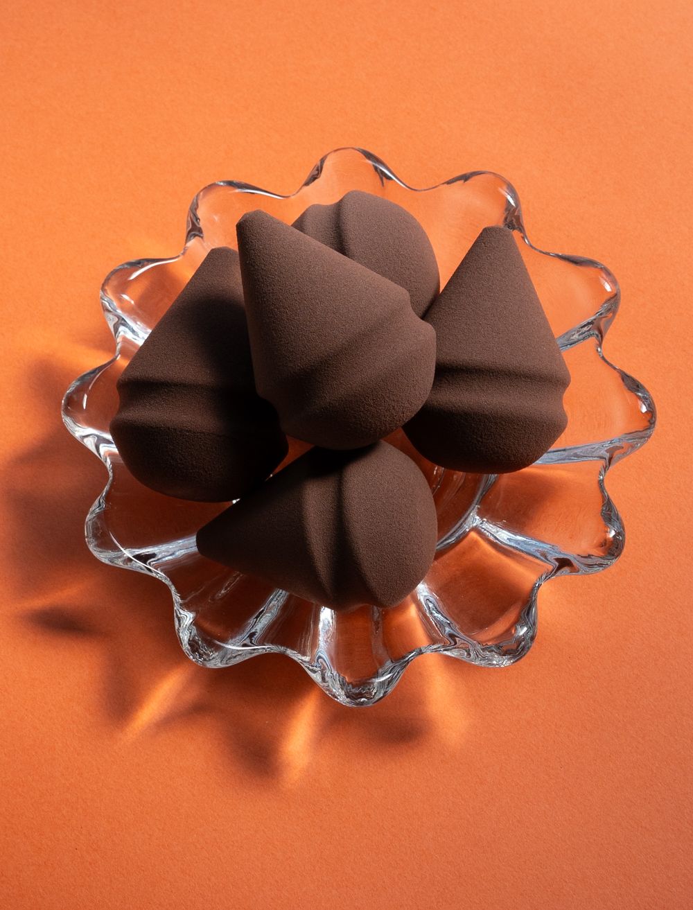 Brown makeup sponges arranged in a crystal glass dish on orange background.