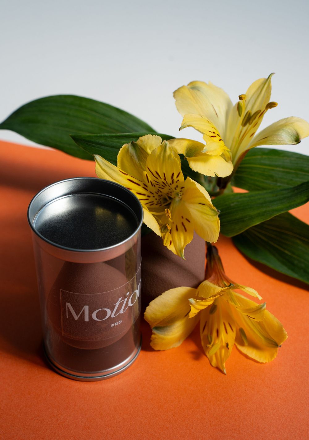 Motion branded container with yellow alstroemeria flowers on orange surface.