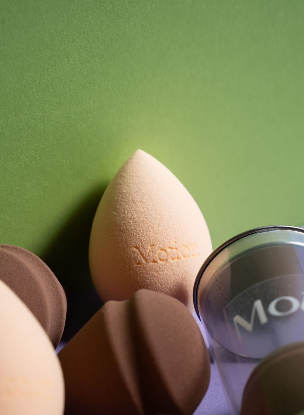 Close-up of a peach-colored makeup sponge with Motion branding against a green background.
