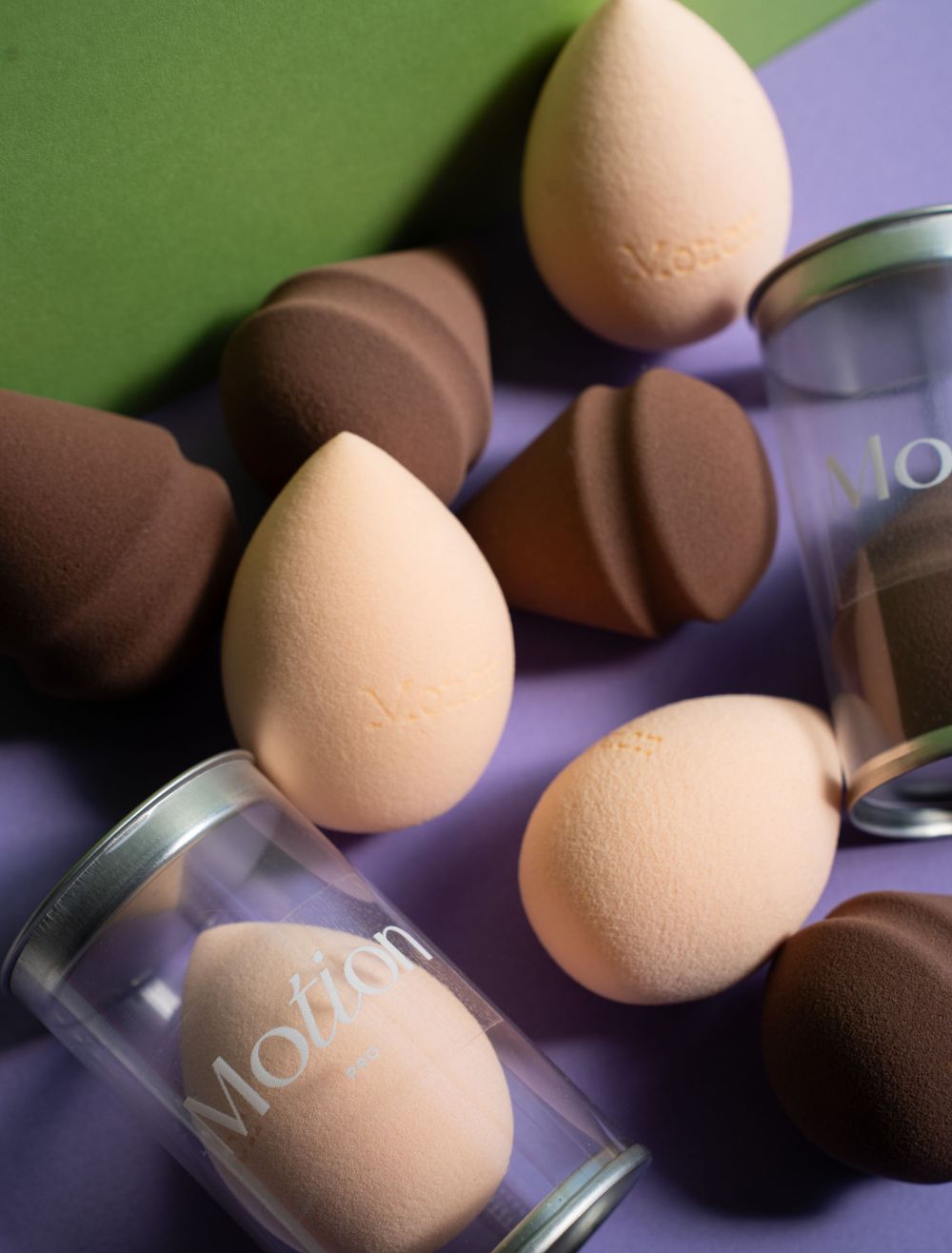 Makeup beauty blenders and applicator sponges in beige and brown tones arranged with glass containers labeled Motion.