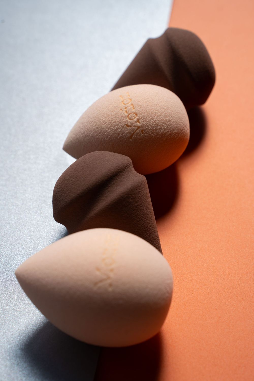 Beauty sponges arranged in diagonal line showing texture and contrast against split-toned background.