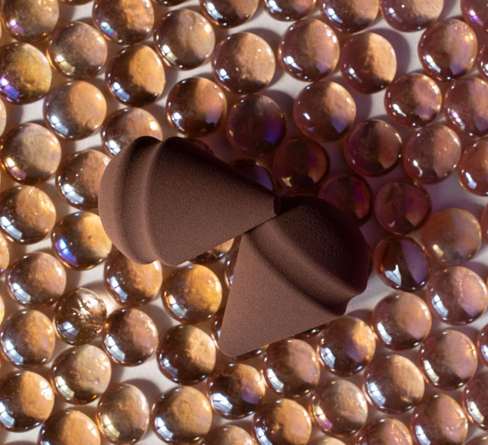 Brown teardrop-shaped makeup sponge surrounded by golden decorative beads in artistic arrangement.