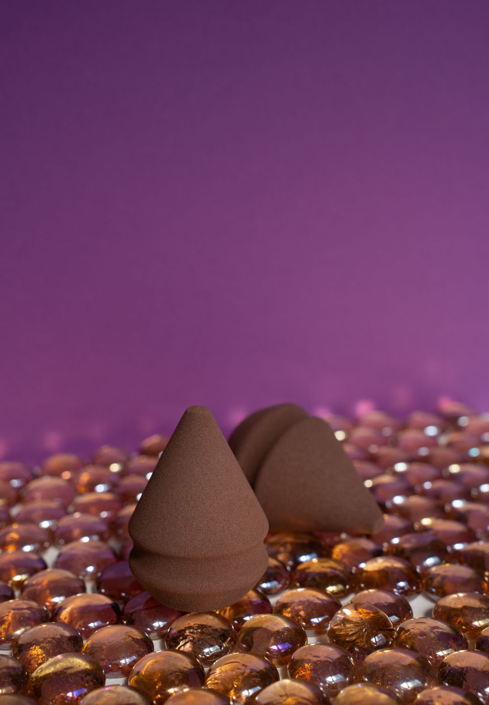 Brown cosmetic sponges positioned on reflective golden beads against purple background.