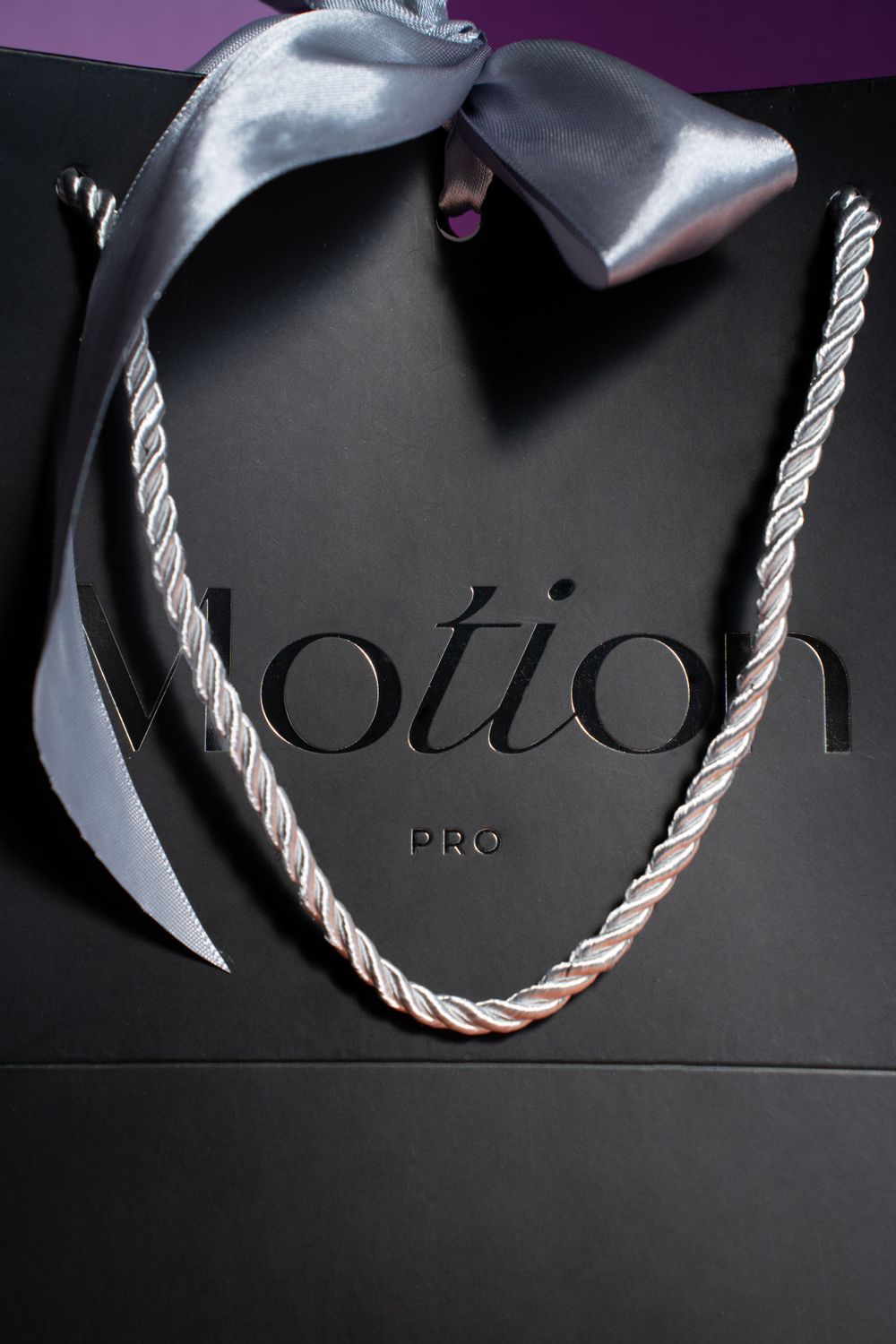 Black retail bag with silver ribbon and 'Motion Pro' branding against a purple background.