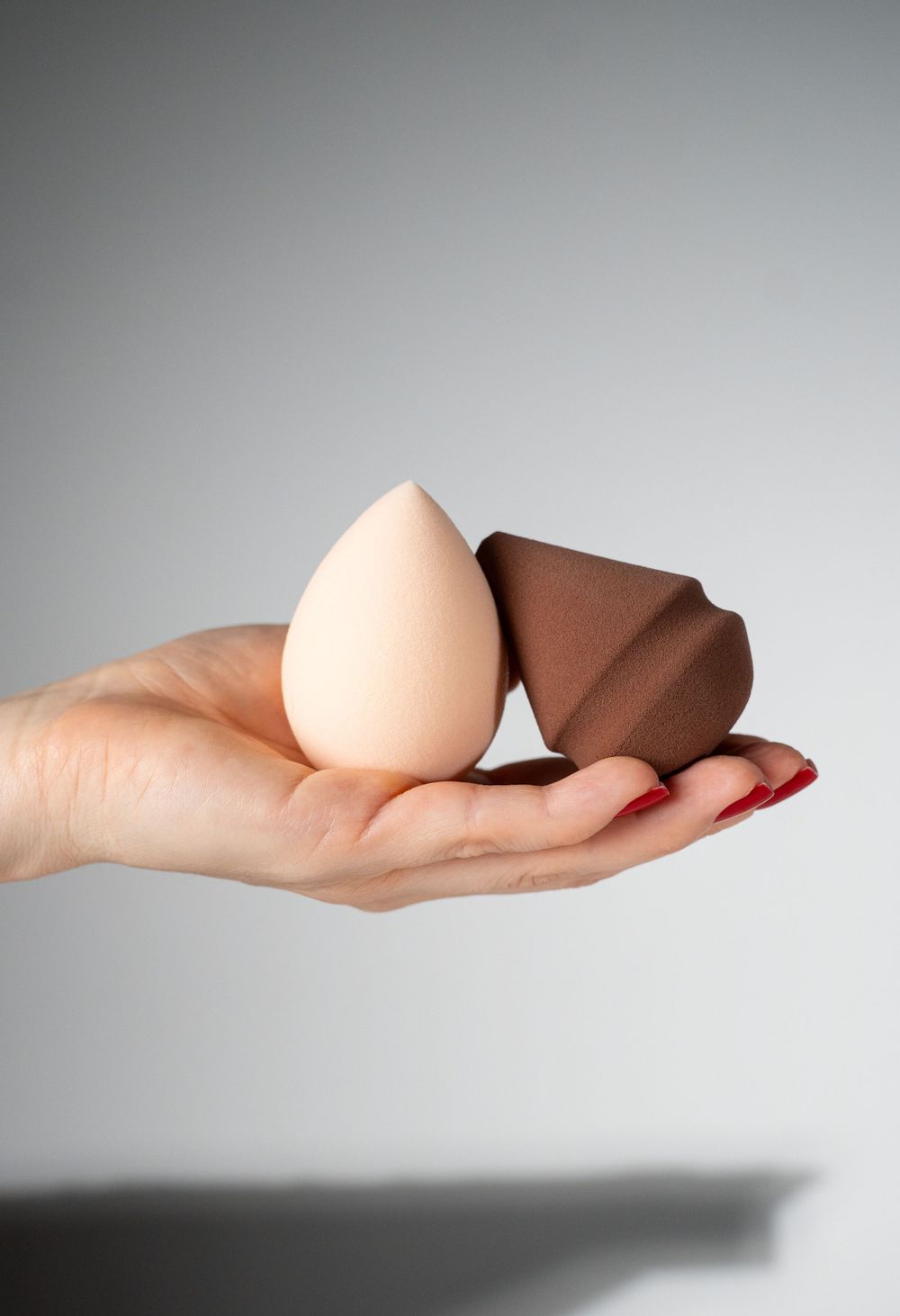 Hand displaying beige and brown makeup sponges against gray background.