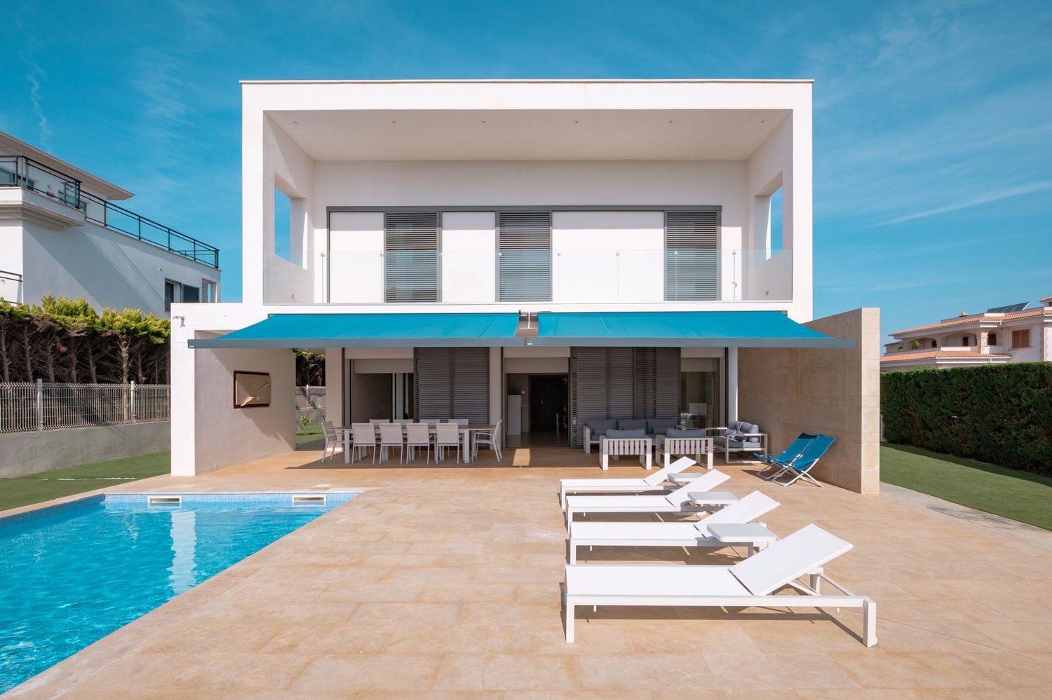 Contemporary white villa with swimming pool and sun loungers on a sunny terrace.