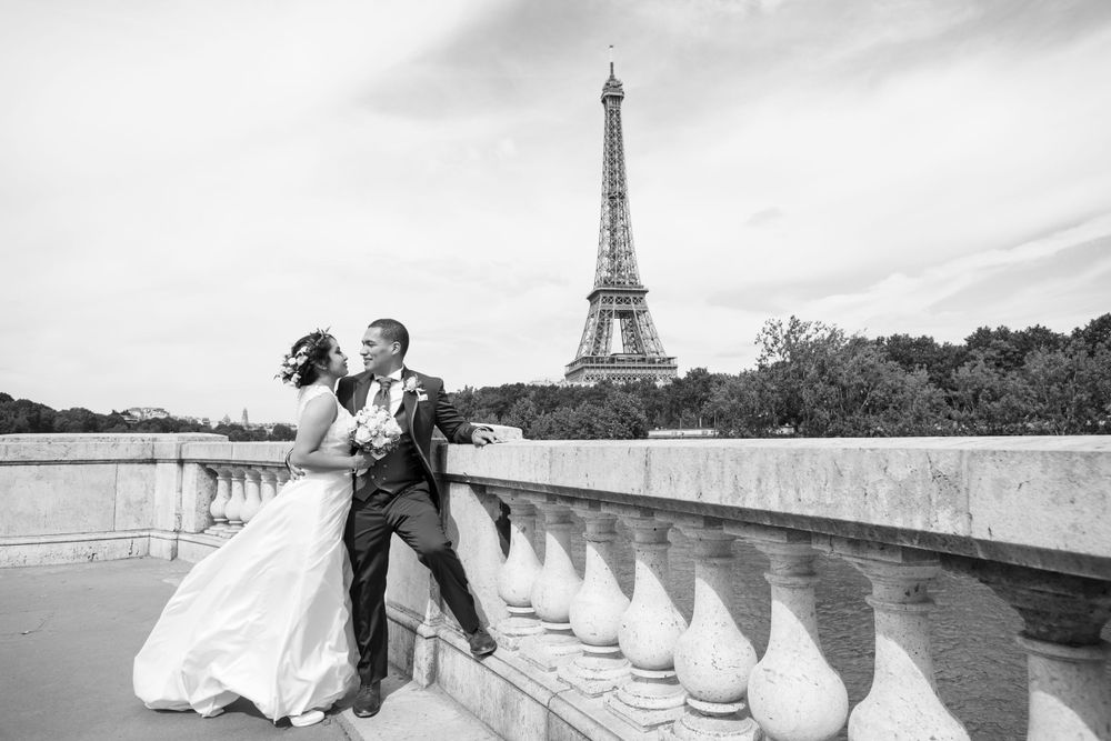 A romantic couple poses on a bridge with the iconic Eiffel Tower visible in the background in Paris, France.