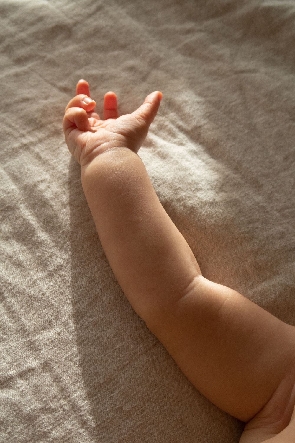 Baby's tiny hand resting on textured fabric in natural lighting.