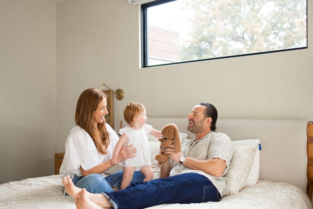 Family relaxing together on a white bed in natural light.