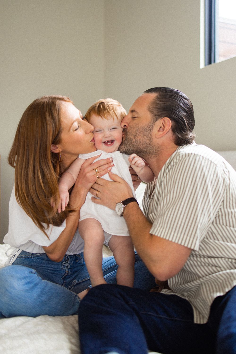A joyful family moment as parents kiss their laughing baby on both cheeks.