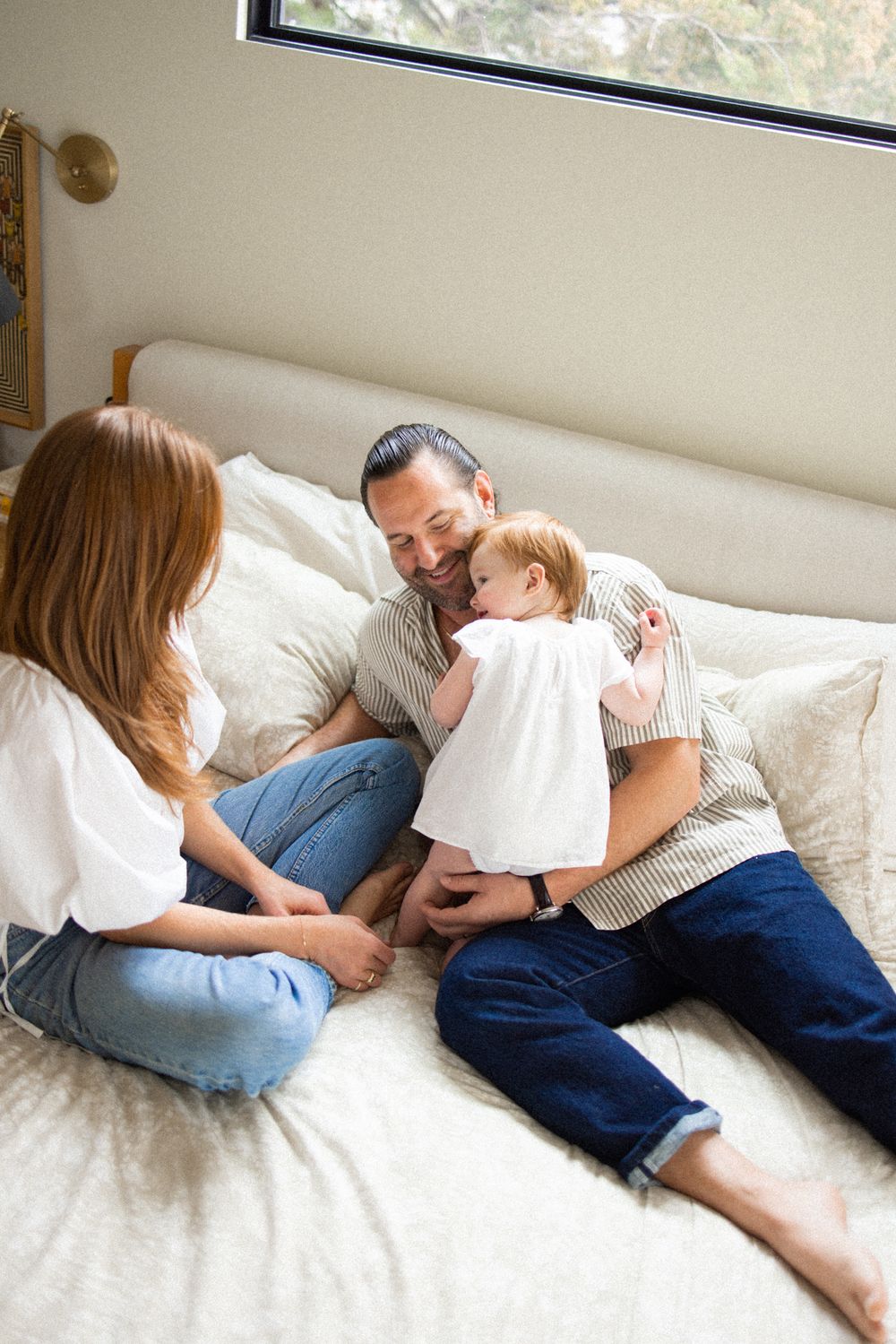 Family lounging together on a white bed in casual clothing.
