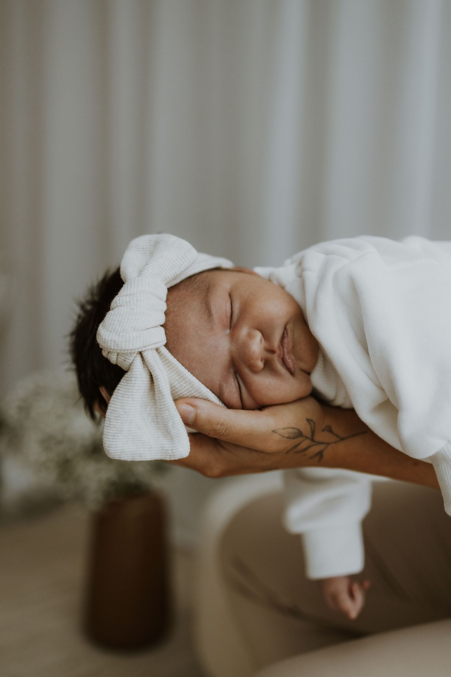 Sleeping newborn wrapped in soft white blanket with bow headband.
