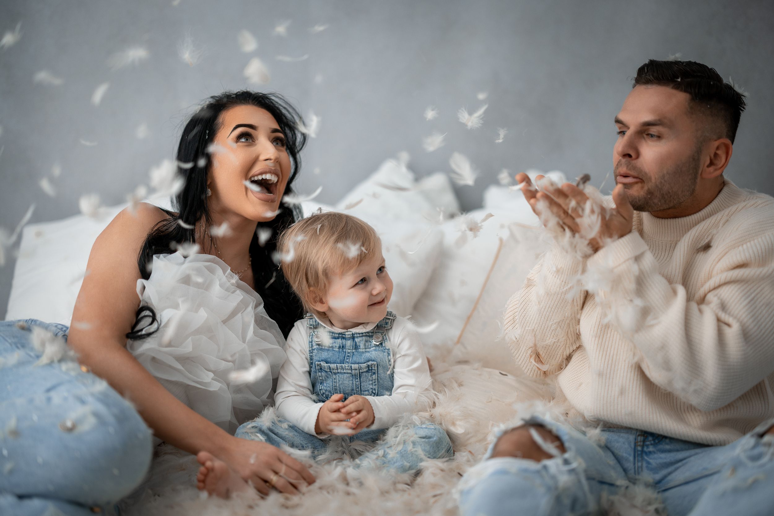 A playful family moment captured with white feathers floating in the air.