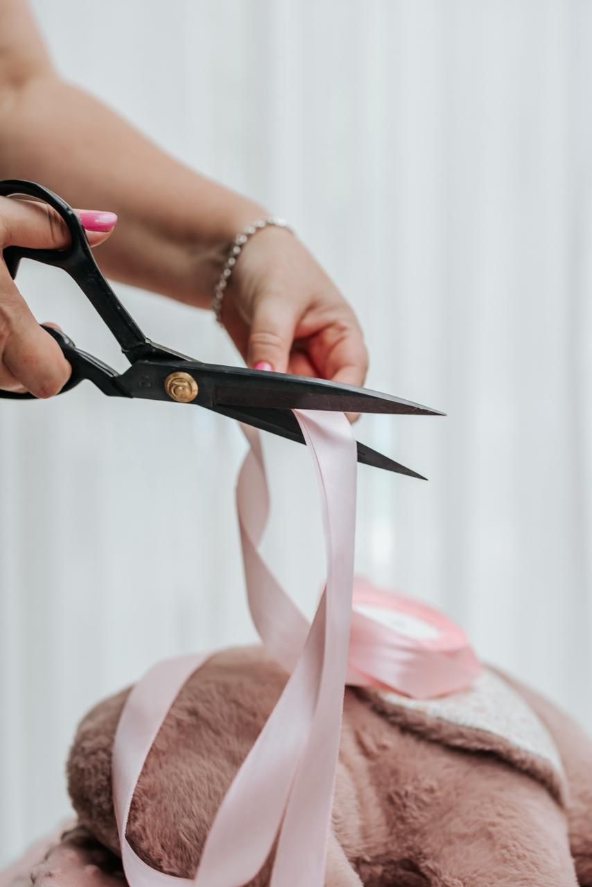 Black scissors cutting through a pink ribbon on a plush brown fabric surface.