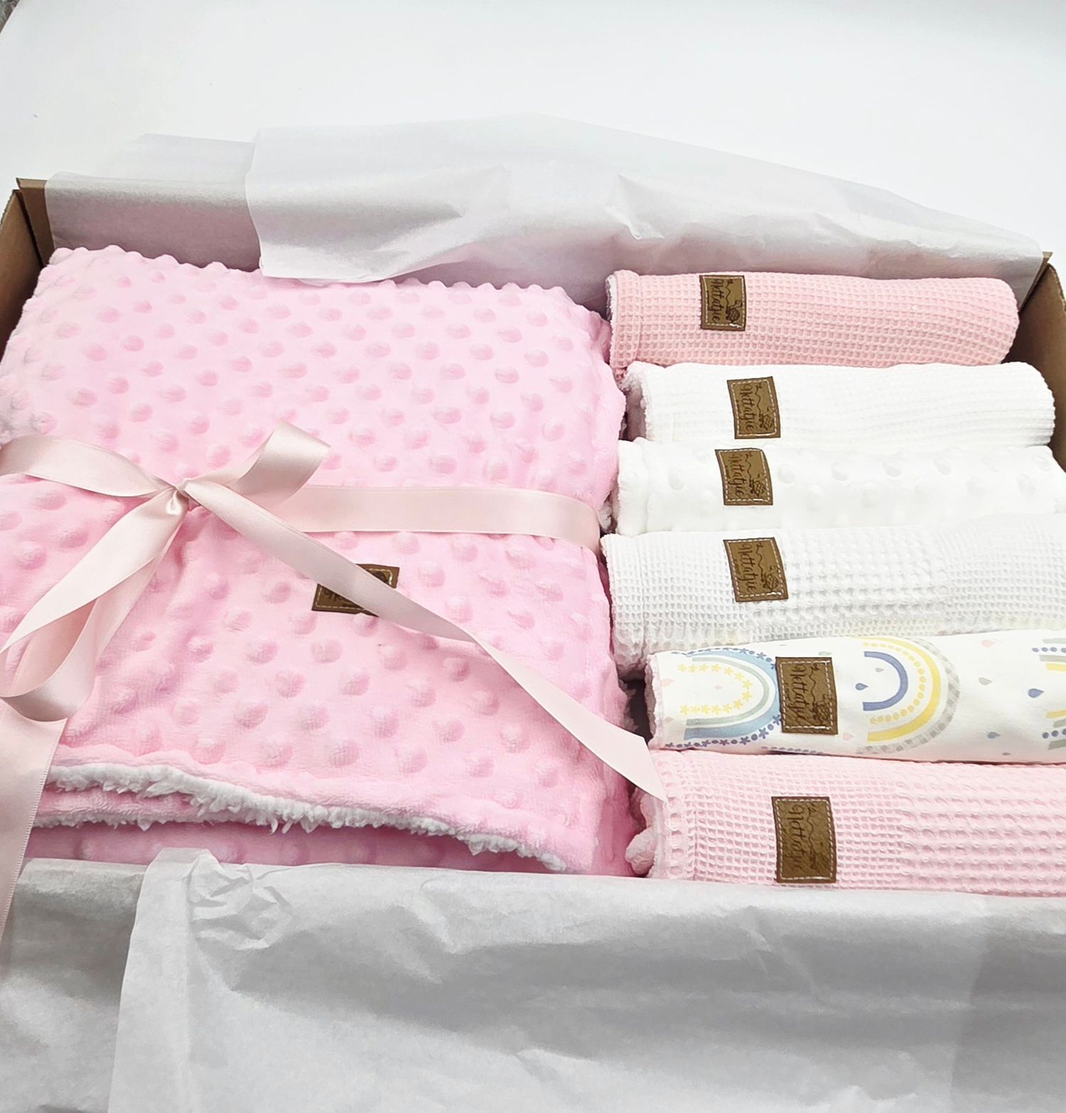 Pink and white baby gift box featuring minky blankets and knit fabrics with rainbow patterns.