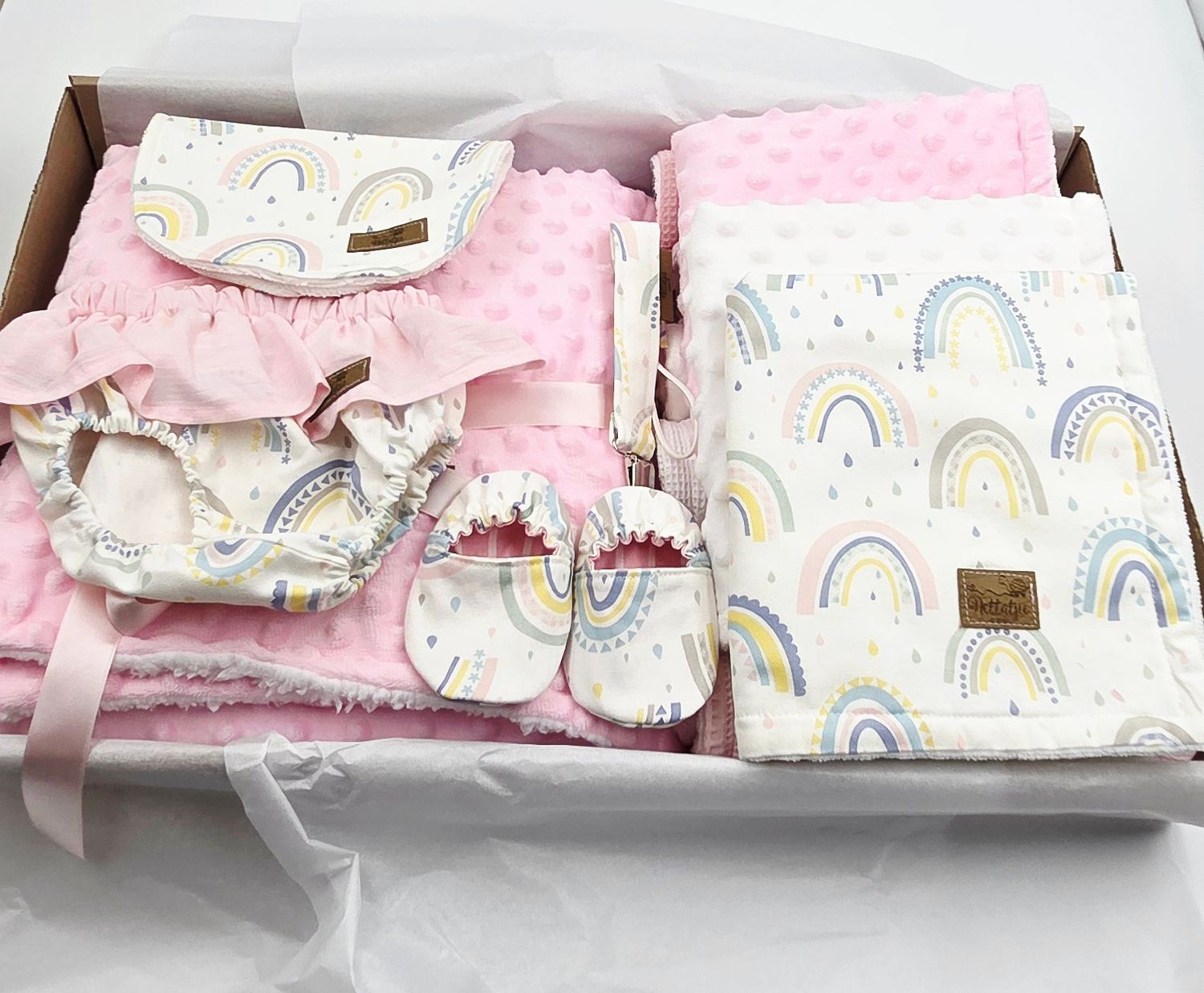 Pink and white baby gift set with rainbow pattern blankets and accessories arranged in a box.