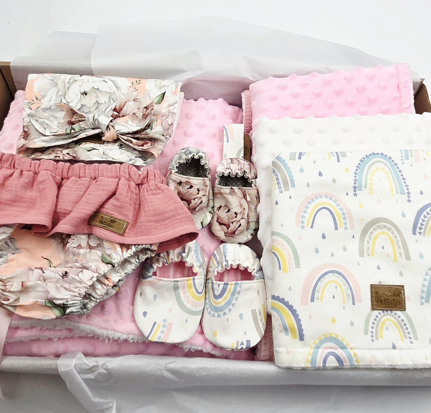 Baby clothing set featuring pink ruffled items, rainbow print blankets, and matching accessories.