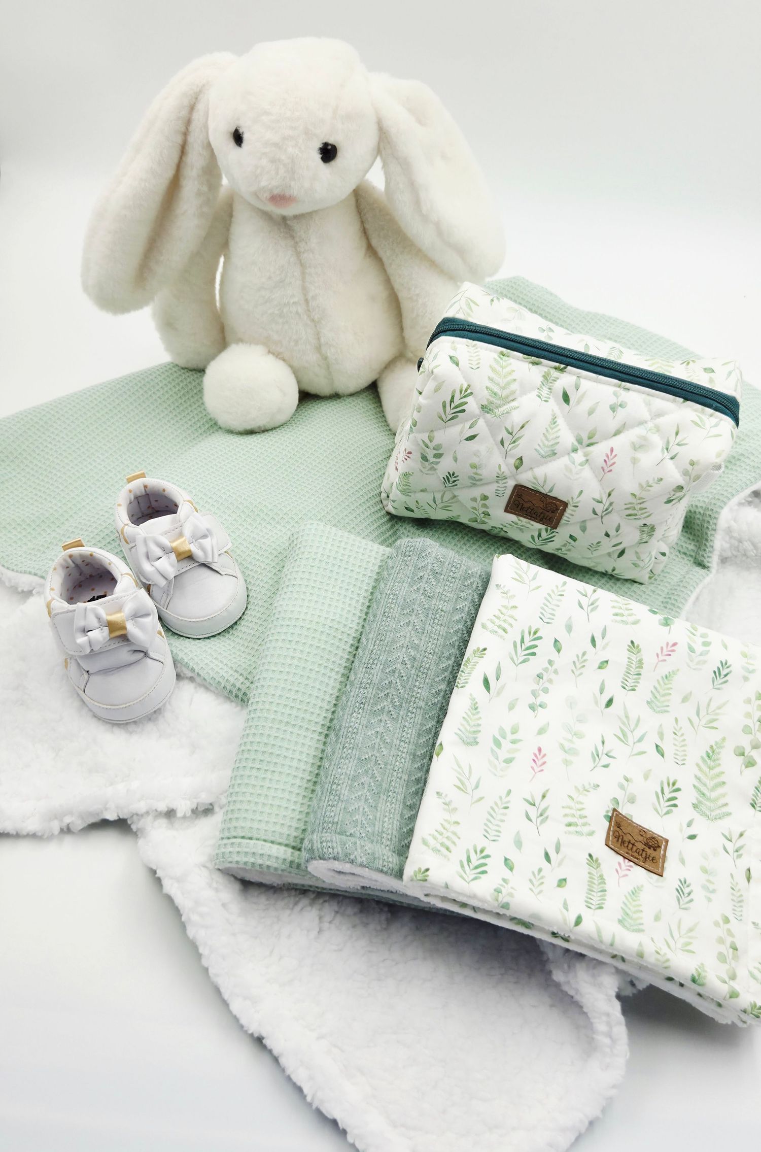 Soft mint green baby accessories with plush bunny, floral prints and tiny gray shoes.