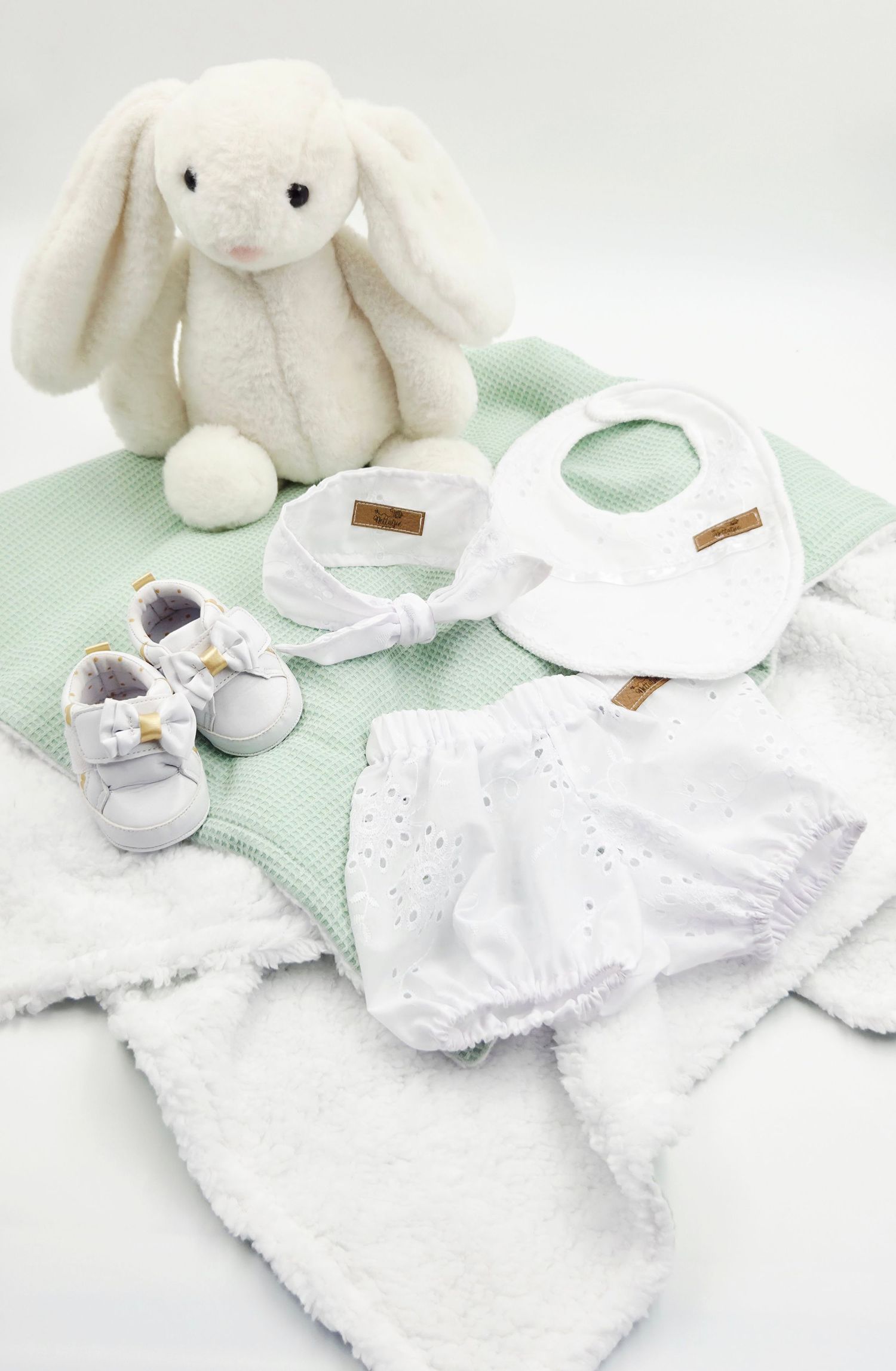 White plush bunny with mint green baby essentials including bibs, shoes and blankets.