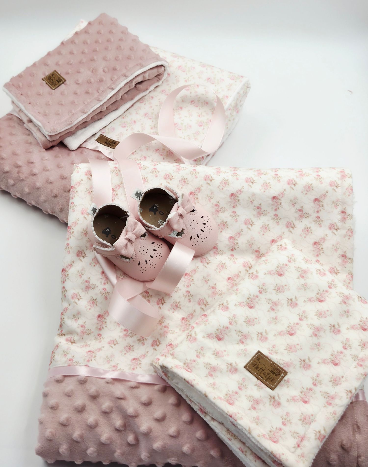 Pink baby set featuring soft textured blankets and tiny rose-colored shoes with floral patterns.