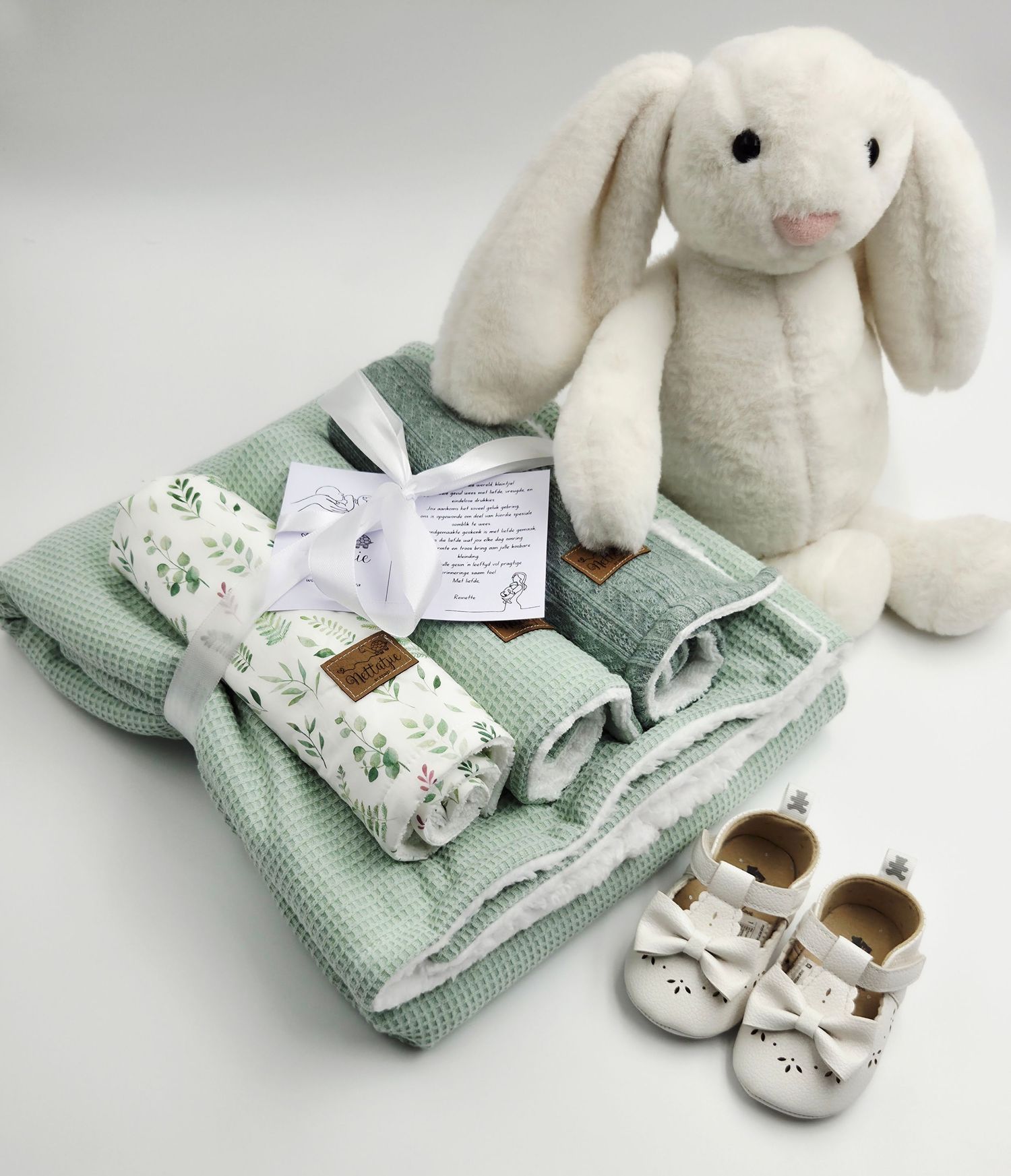 White plush bunny displayed with mint green baby blankets and tiny shoes.