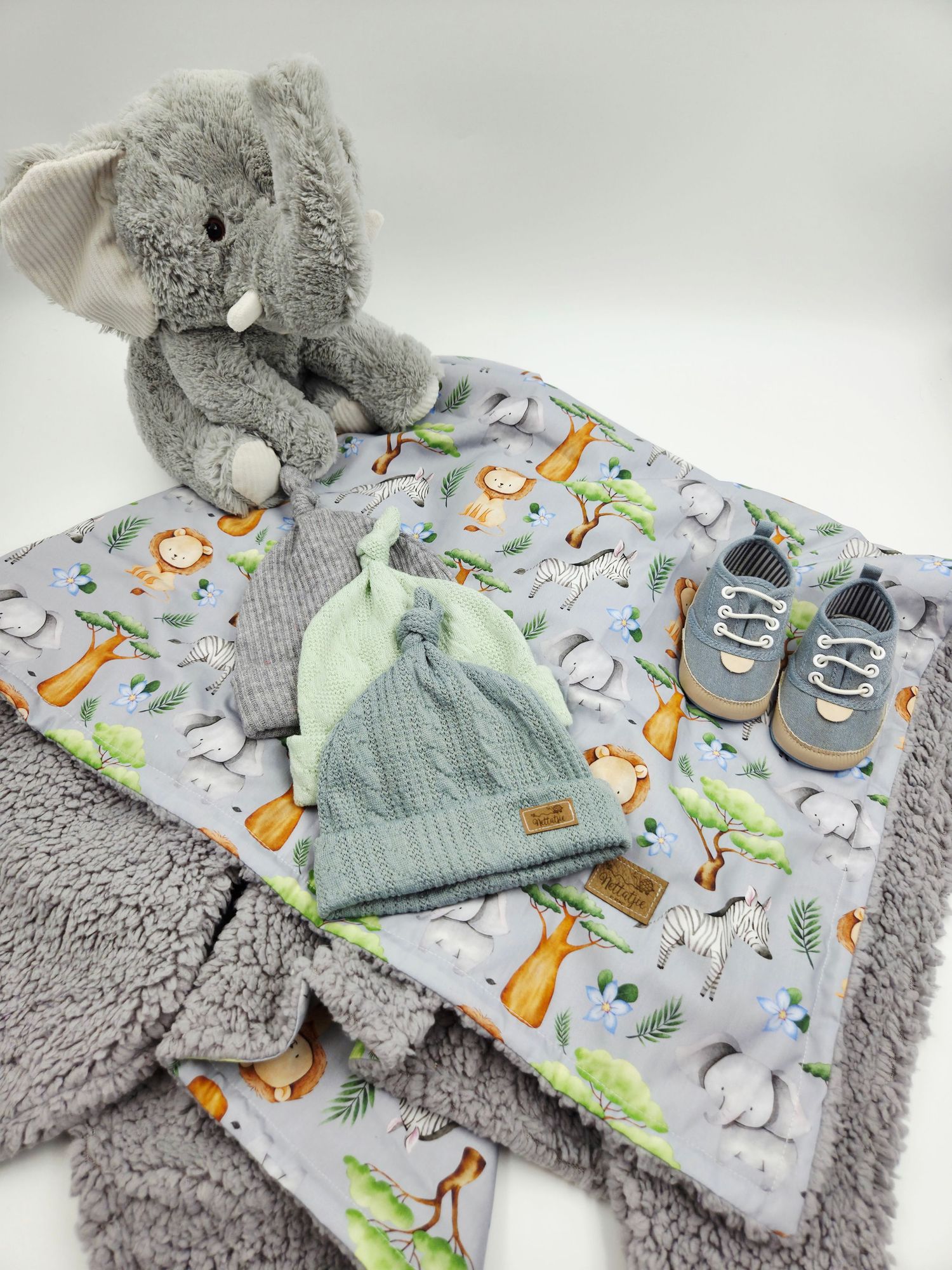 Grey plush elephant with safari print baby blanket and mint green accessories.
