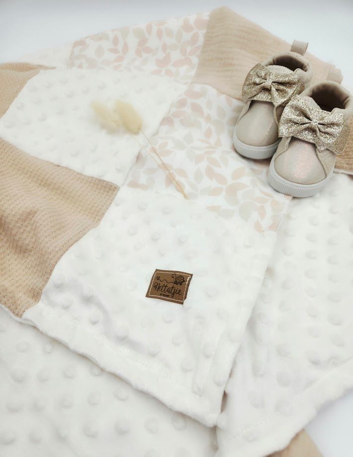 Soft cream and beige minky baby blanket with leaf pattern, paired with gold bow baby shoes on white background.