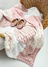Pink floral baby blanket with minky dots and soft shoes displayed on a wicker chair.