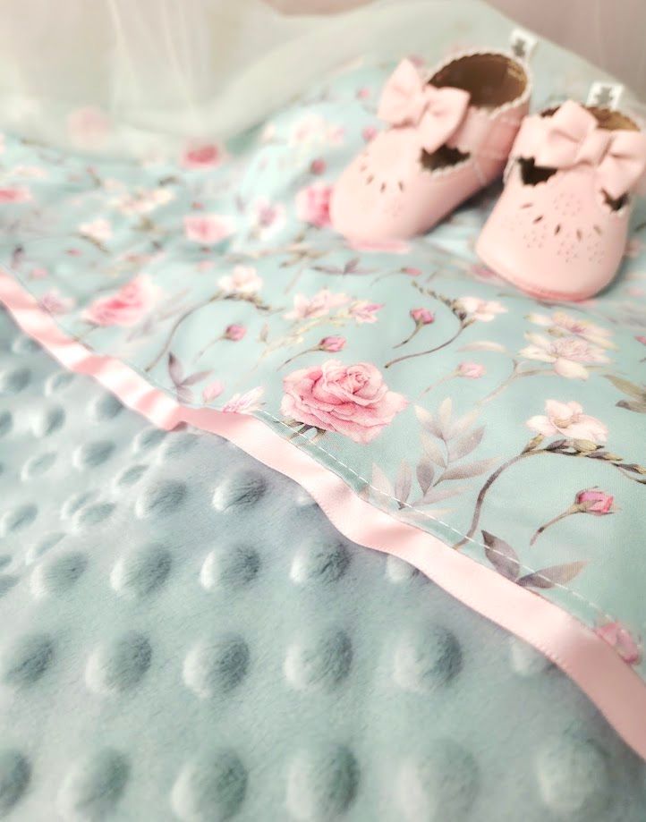 Mint green floral baby blanket with pink rose pattern and matching pink bow baby shoes on soft textured minky fabric.