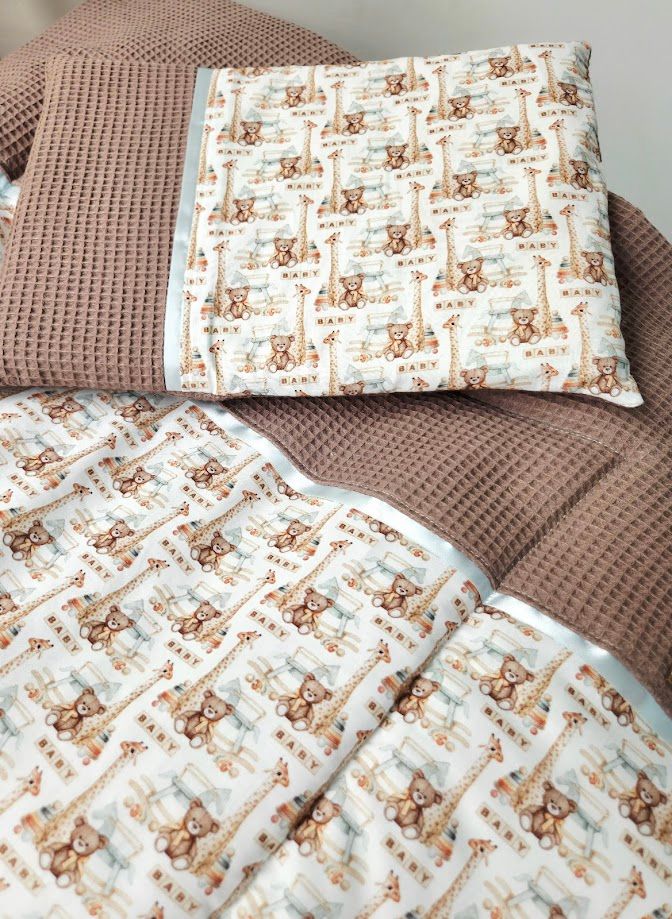 Baby bedding set with cute giraffe and bear pattern, paired with a brown waffle-knit blanket on a cozy chair.