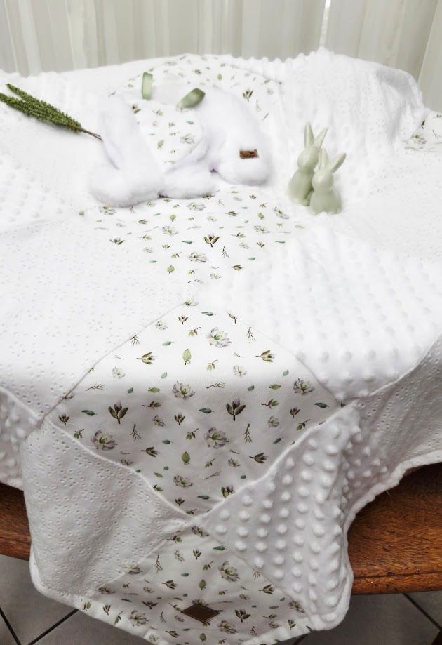 White minky dot baby blanket with floral print panels, displayed with bunny toys and greenery on a wooden chair.