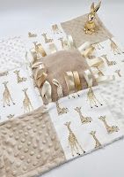 Soft baby sensory blanket with giraffe print fabric squares, minky dot texture, and satin ribbon tags in neutral beige tones.
