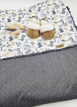 Baby sleeping bag set with dinosaur print fabric and gray quilted blanket, displayed with small slippers.