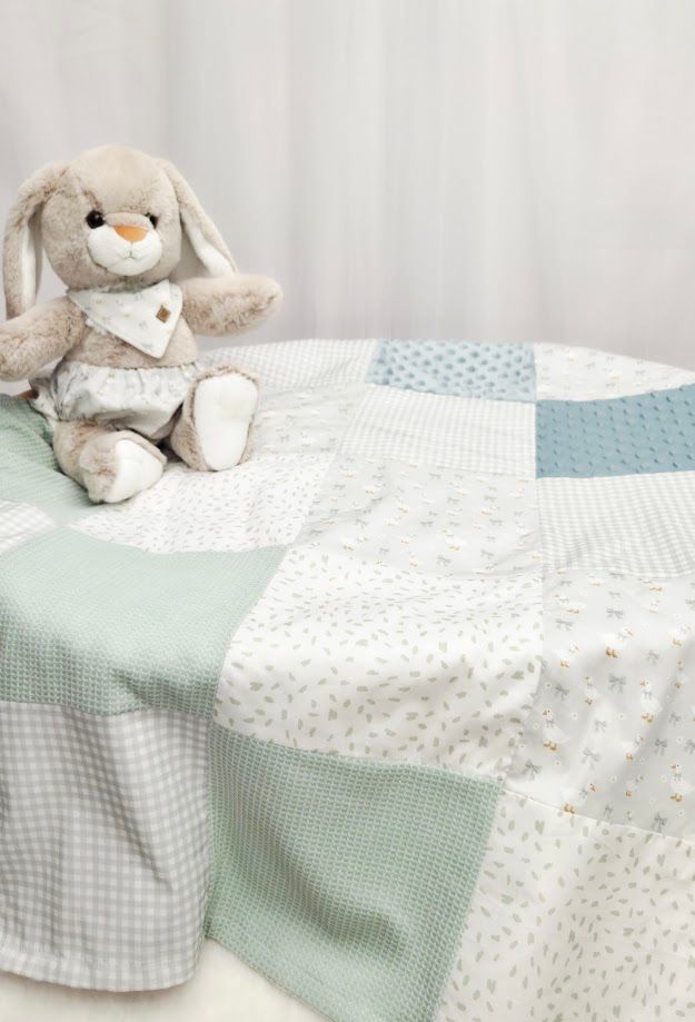 Soft patchwork baby quilt in mint green and white with a plush bunny stuffed animal on a cozy bed.