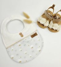 White waffle knit baby bib with gold dot print paired with tan leather sandals with floral accents.