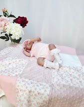Newborn baby sleeping on a pink floral patchwork quilt beside a bouquet of pink and red flowers.