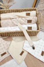 Neutral beige baby gift set with muslin cloths, bibs, and pacifier clip in a woven basket.