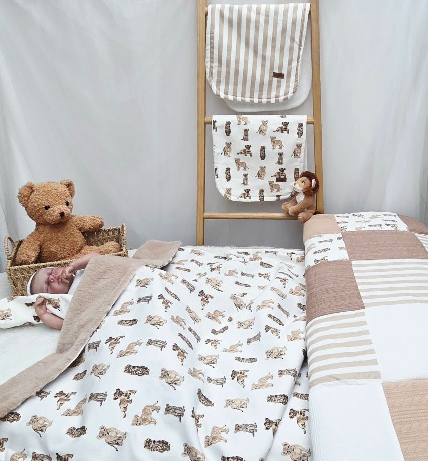 Neutral-toned baby bedding set with animal prints, patchwork quilt, striped blankets, and teddy bear on a wooden ladder display.