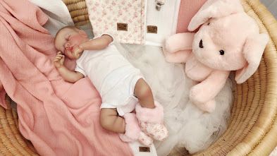 Newborn baby sleeping in a wicker basket with a pink blanket and soft plush bunny toy.