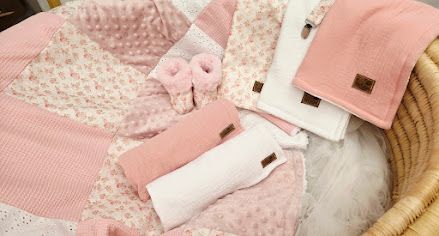 Pink and white baby gift set with patchwork quilt, booties, hat, and blankets in a wicker basket.