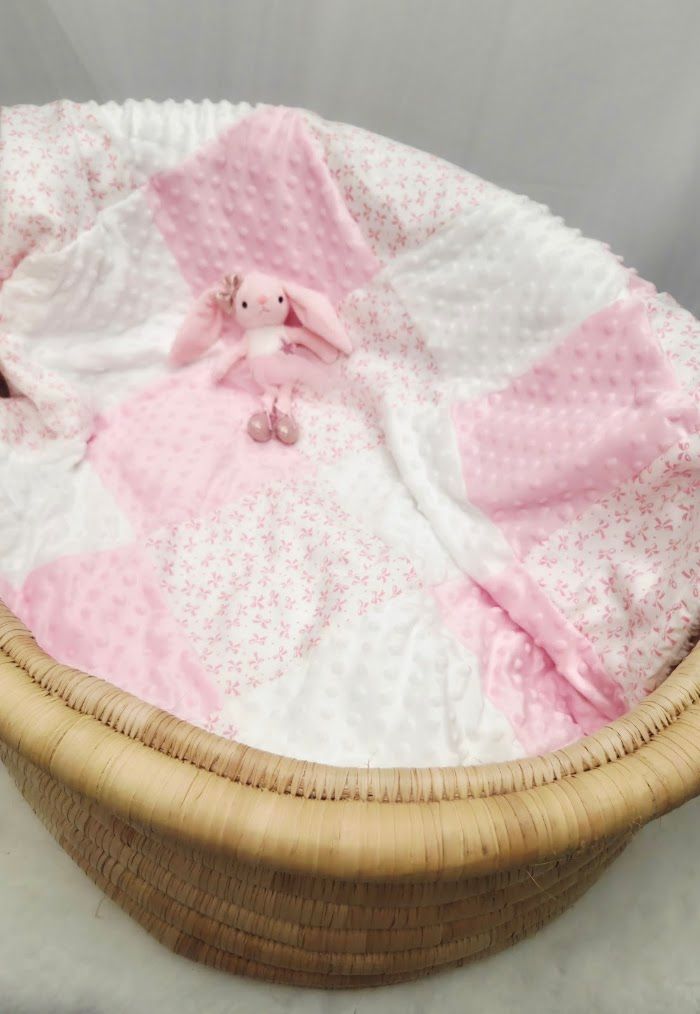 Pink patchwork baby quilt with bunny stuffed animal in a woven moses basket.